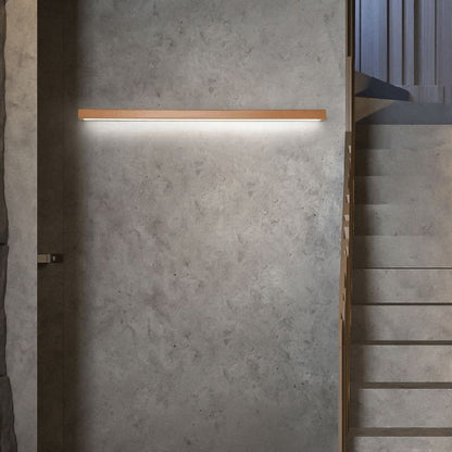 Applique murale linéaire Dimoree en bois naturel avec éclairage LED chaud installée sur un mur en béton gris