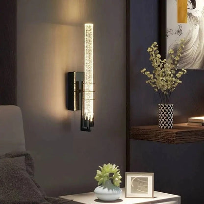 Applique murale Dimoree moderne en cristal cylindrique avec support noir diffusant une lumière chaude dans un salon
