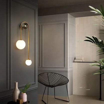 Applique murale Dimoree moderne à deux sphères en verre opalin et métal doré sur un mur gris élégant