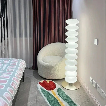 Lampadaire design Dimoree en acrylique blanc empilé, diffusant une lumière douce dans une chambre contemporaine.