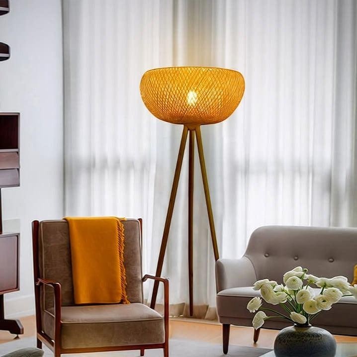Lampadaire trépied Dimoree en bambou tressé diffusant une lumière douce dans un salon au style bohème chic.