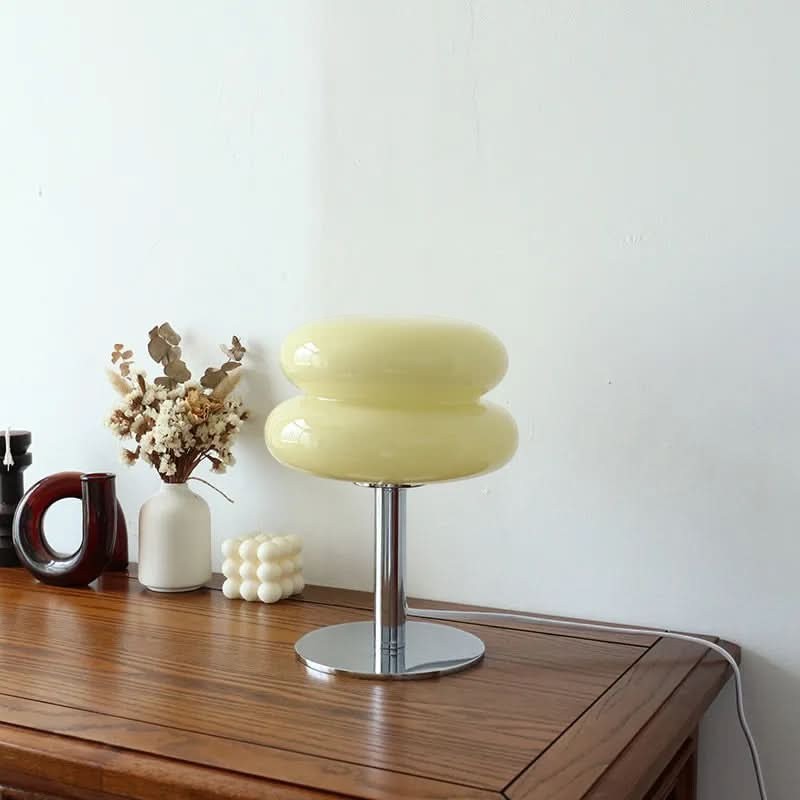 Lampe de table Dimoree en verre soufflé jaune pâle avec pied en métal chromé sur une console en bois.