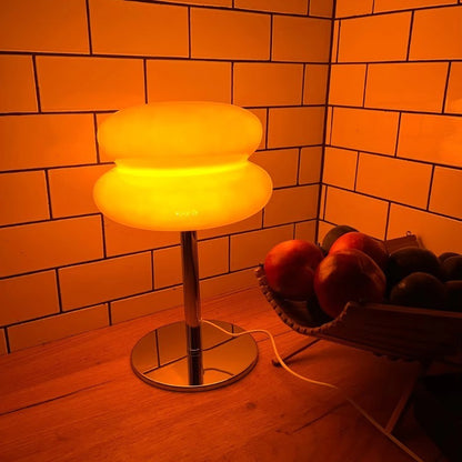 Lampe de table Dimoree en verre soufflé orange en forme de macaron avec pied chromé brillant sur un comptoir en bois