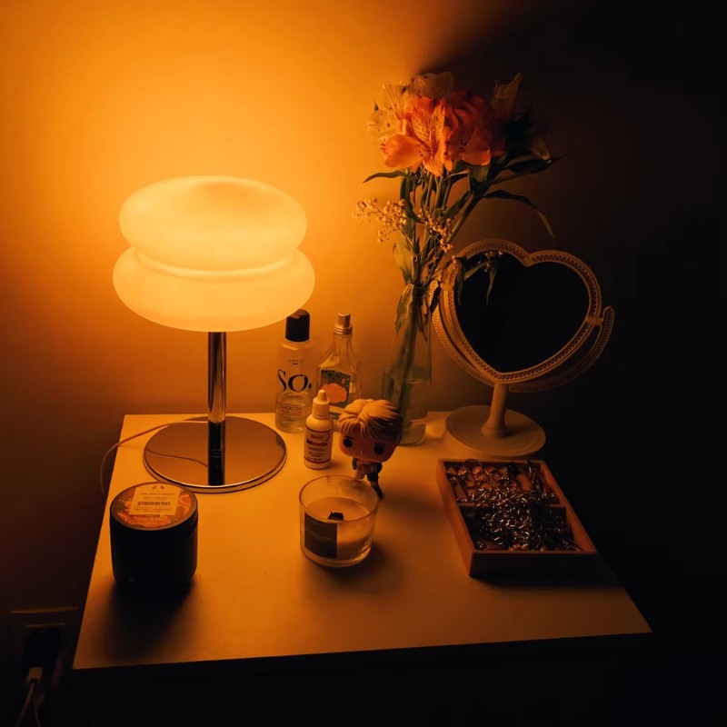 Lampe de table Dimoree en verre soufflé orange avec pied chromé, diffusant une lumière chaude sur une table de chevet.