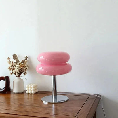 Lampe de table Dimoree en verre soufflé rose, design organique rétro-chic avec pied en métal chromé sur table en bois.