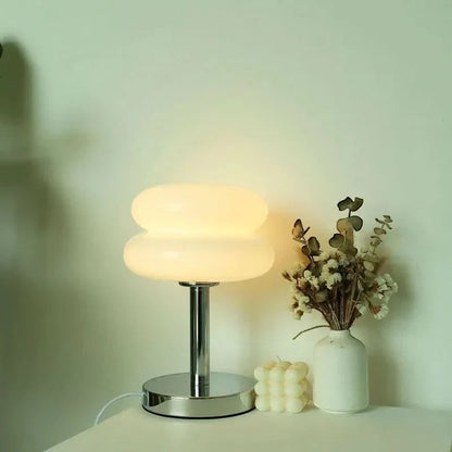 Lampe de table Dimoree en verre soufflé blanc forme macaron avec pied chromé sur une table avec fleurs séchées
