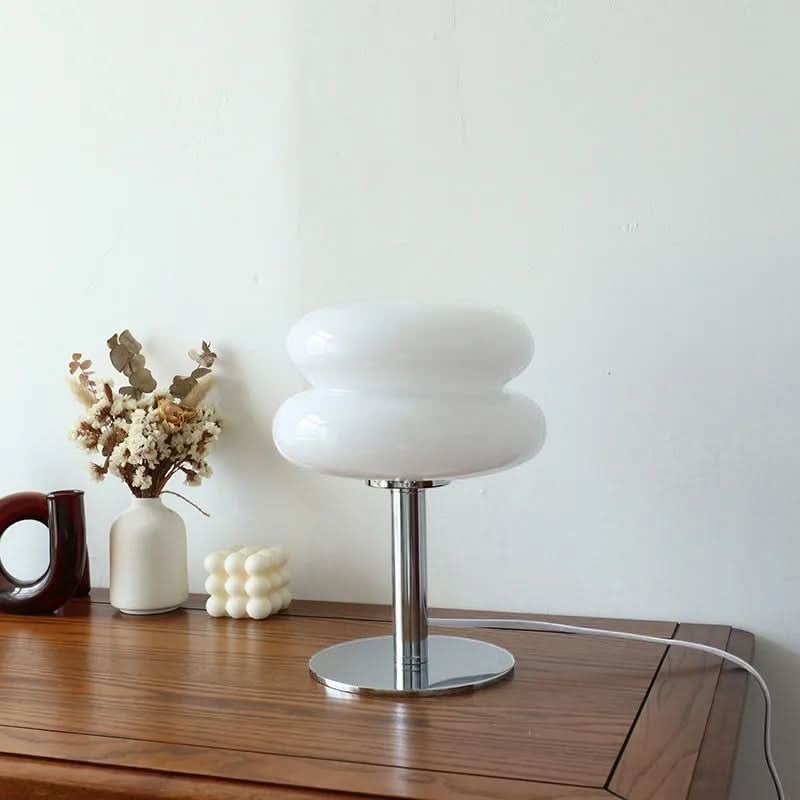 Lampe de table Dimoree en verre soufflé blanc forme macaron avec pied chromé sur une table en bois