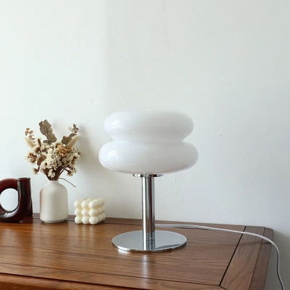 Lampe de table Dimoree en verre soufflé blanc forme macaron avec pied chromé sur une table en bois