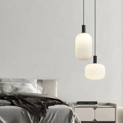 Suspension lumineuse moderne Dimoree en verre dépoli nervuré avec structure en métal noir mat au-dessus d'un lit.
