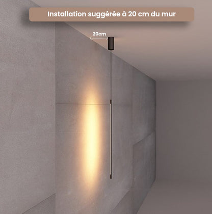 Suspension lumineuse tubulaire Dimoree noire mate au design minimaliste diffusant une lumière chaude sur un mur gris.