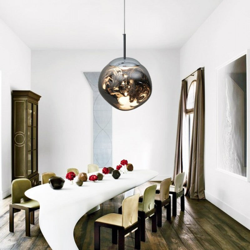 Suspension lumineuse Dimoree en verre soufflé organique avec reflets dorés et ambrés au-dessus d'une table à manger.