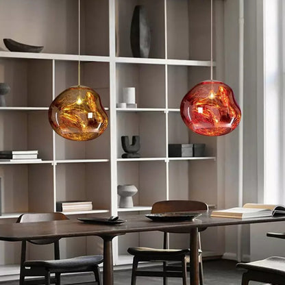 Suspension lumineuse Dimoree en verre soufflé organique aux reflets ambrés et rouges au-dessus d'une table à manger