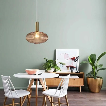 Suspension Dimoree en verre fumé nervuré et métal doré brossé au-dessus d'une table de salle à manger moderne.